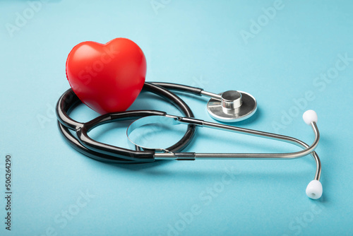 Black stethoscope and red heart on a blue background, close up.Health care. Place for text. Medicine concept. Cardiology concept.