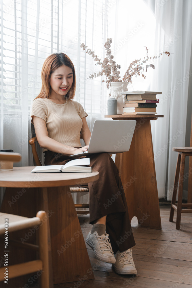 Asian girl. Beautiful woman enjoys chatting on her laptop on the phone in the house next to the window. Asian girl. Beautiful woman enjoys chatting on her laptop on the phone in the house next to the window.