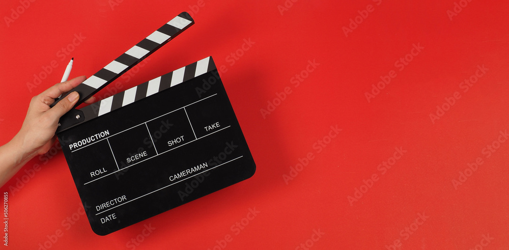Hand is holding black clapper board with Marker Pen on red background.