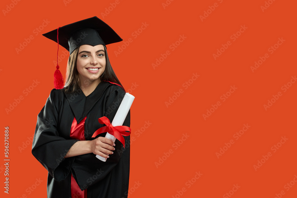 Front view of brunette girl standing with crossed hands, holding diploma. Pretty young woman graduating from college, university, high school. Isolated on red studio background. Front view of brunette girl standing with crossed hands, holding diploma. Pretty young woman graduating from college, university, high school. Isolated on red studio background.