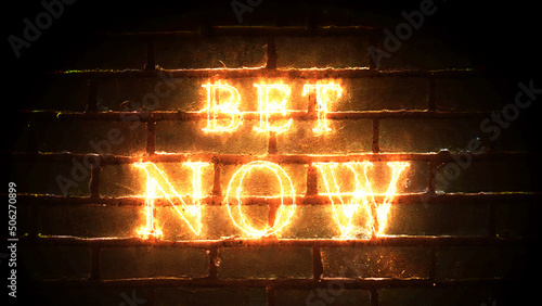 Fotografija Bet Now glowing fiery inscription on brick wall background