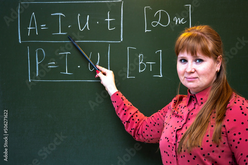 A physics teacher stands near the blackboard where formulas for physics are written.