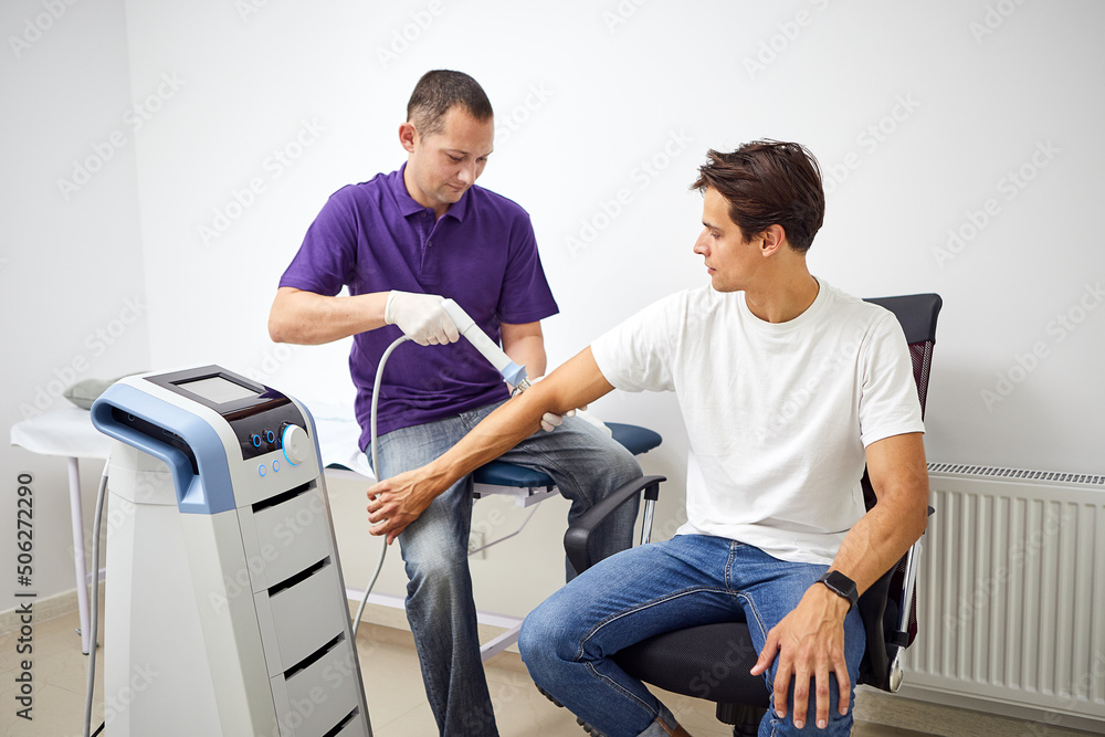 Obraz premium Shock wave therapy. Physiotherapist doctor uses medical equipment for highly effective epicondylitis, pain and inflammation treat. Concept of medical joint treatment