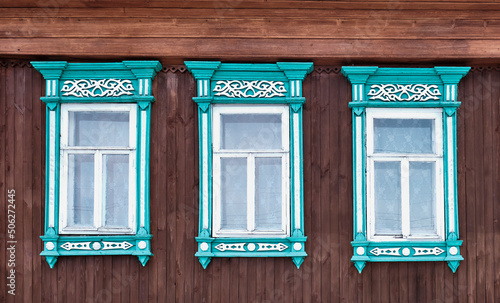 Tableau sur toile Three old windows with wooden turquoise architraves with patterns on brown board wall
