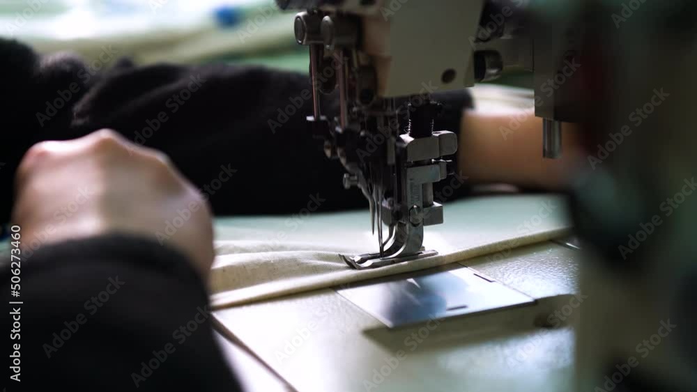 Women's hands sew a stitch on a sewing machine. Industrial sewing machine. Change of focus close-up of the foot of a working sewing machine Women's hands sew a stitch on a sewing machine. Industrial sewing machine. Change of focus close-up of the foot of a working sewing machine