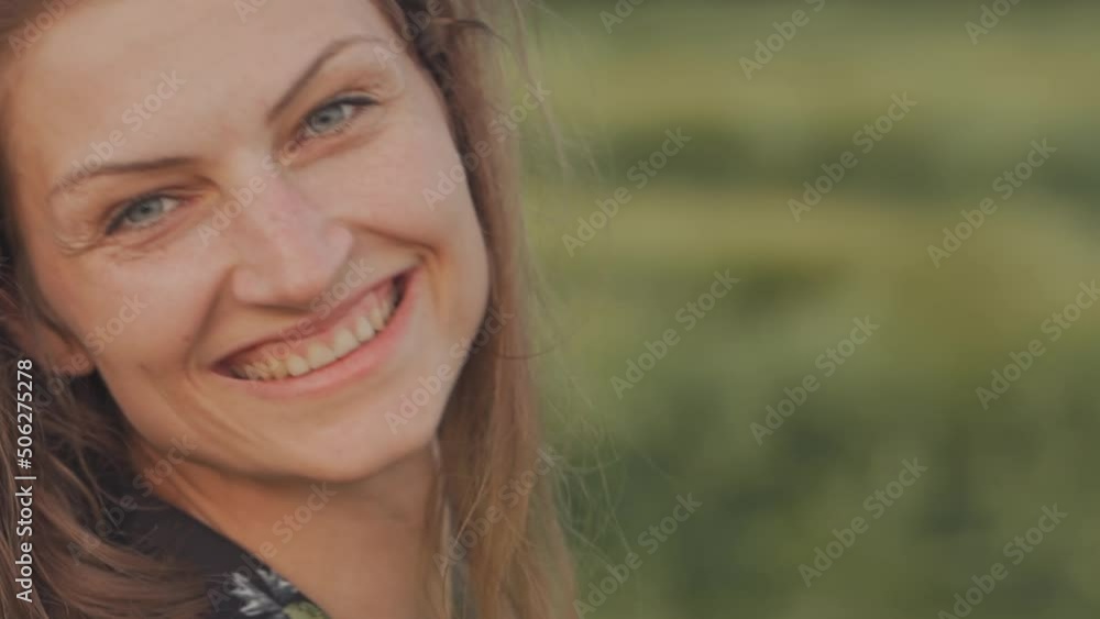 Young happy woman with flowing hair and blue eyes in a summer dress in a wheat field, gently touches a spikelet of wheat, smiles and looks at the camera. Young happy woman with flowing hair and blue eyes in a summer dress in a wheat field, gently touches a spikelet of wheat, smiles and looks at the camera.