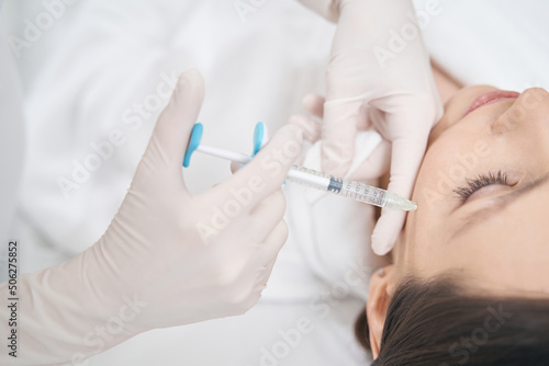 Beautician making rejuvenating facial injection in female cheek