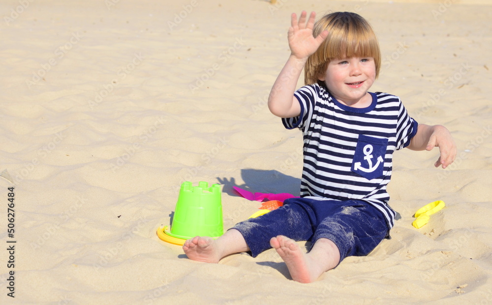 The kid plays with a bucket and a shovel in the sand. Little boy sailor on the beach. The kid plays with a bucket and a shovel in the sand. Little boy sailor on the beach.
