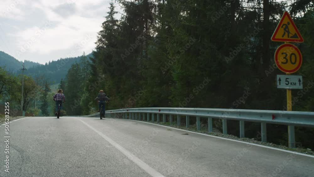 Sporty couple cycling forest on highway road. Travelers riding bike in mountains Sporty couple cycling forest on highway road. Travelers riding bike in mountains