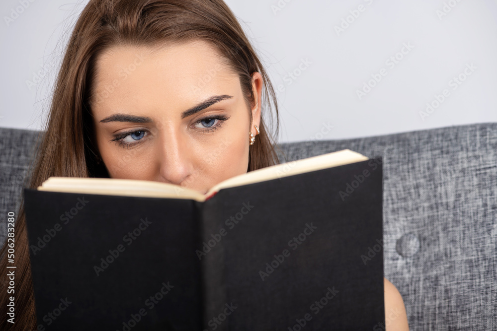 Leisure and hobbies concept. Portrait of beautiful brunette woman with blue eyes reading book. Book with blank black old and aged cover and copy space. Model eyes looking to book Leisure and hobbies concept. Portrait of beautiful brunette woman with blue eyes reading book. Book with blank black old and aged cover and copy space. Model eyes looking to book