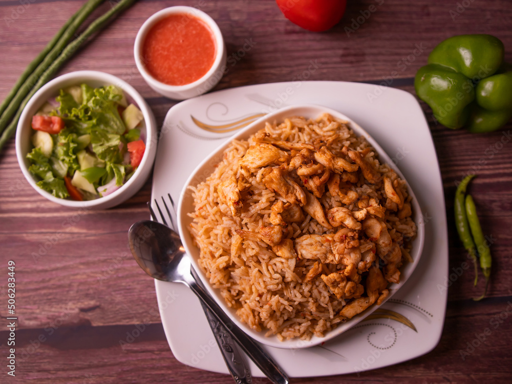 Spicy Indian chicken pulao with salad, sauce and spoon in a dish top view on wooden background pakistani chicken biryani Spicy Indian chicken pulao with salad, sauce and spoon in a dish top view on wooden background pakistani chicken biryani