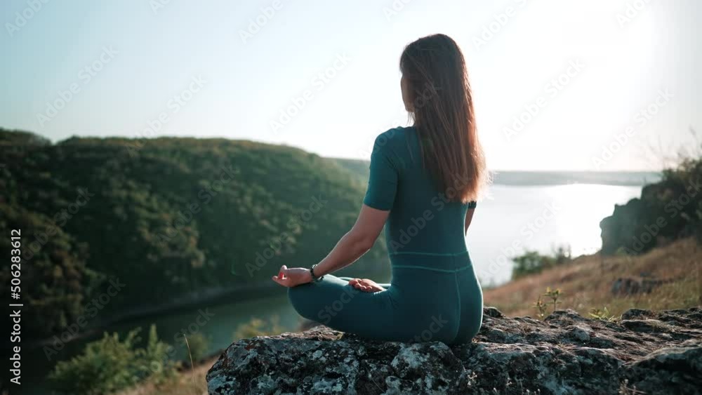Unrecognizable concentrated woman in lotus pose meditating on high rock above water. Calm yoga concept, zen, relaxation, practice on nature background. Unrecognizable concentrated woman in lotus pose meditating on high rock above water. Calm yoga concept, zen, relaxation, practice on nature background.
