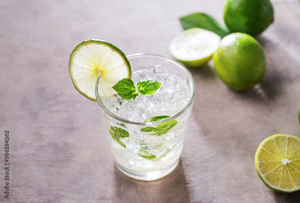 Fototapeta premium Refreshing mojito cocktail with mint and lime in a glass with ice on pink background with morning shadows. Concept summer citrus drink and fruits. Copy space