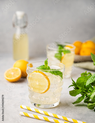 Lemonade soda drink with fresh lemons. Refreshing cocktail with lemon, mint and ice on textured light background. Summer cold drinks concept