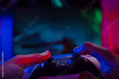 Close-up. The gamer holds a gamepad in his hands. Plays video games online with friends. Neon lighting. Technological background. Game strategy, cyberspace, esports.