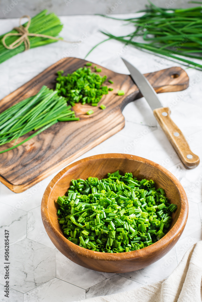 Fresh chopped green onions in a wooden bowl and a cutting board on the table. Vertical view
