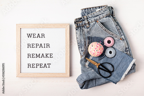 Jeans with letter board and text wear, repair, remake, repeat. Slow fashion, circular economy, eco friendly sustainable shopping, thrifting second hand shop concept.