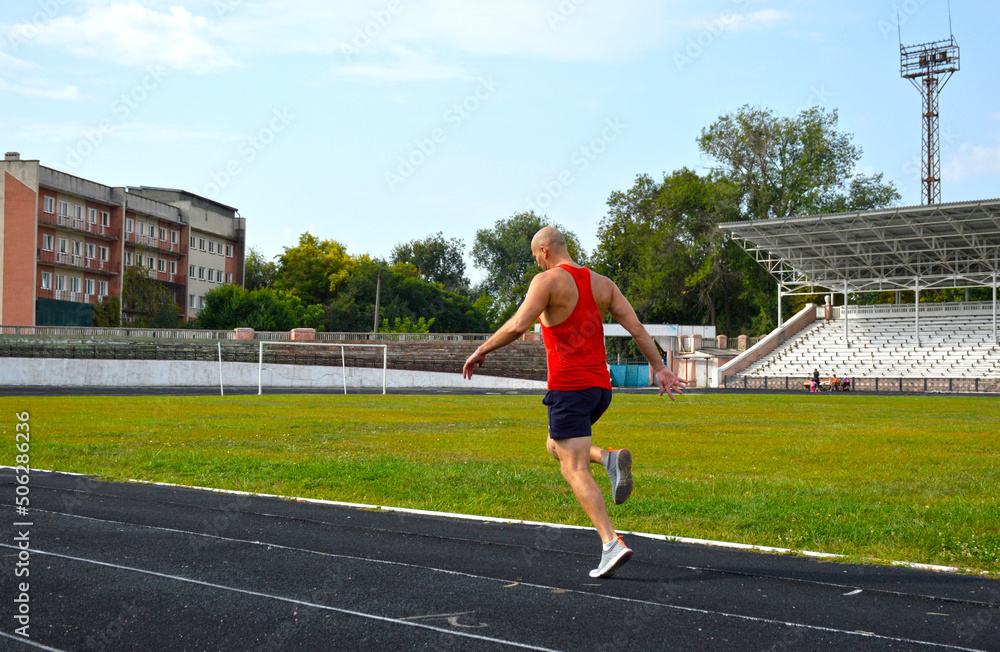 Fototapeta premium young muscular athlete runs on a black rubber treadmill in the stadium. outdoor training. active lifestyle and sports