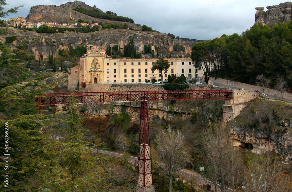 View of the monastery Antiguo Convento de San Pablo and the iron bridge Puente de San Pablo with mountains in the background in Cuenca, near Madrid, Spain