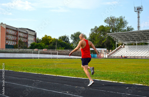 young muscular athlete runs on a black rubber treadmill in the stadium. outdoor training. active lifestyle and sports