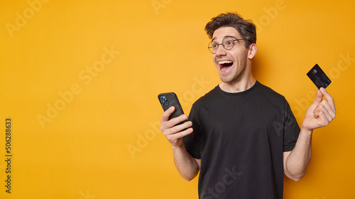 Fotografie Cheerful handsome guy wears spectacles and casual black t shirt glad to get sala