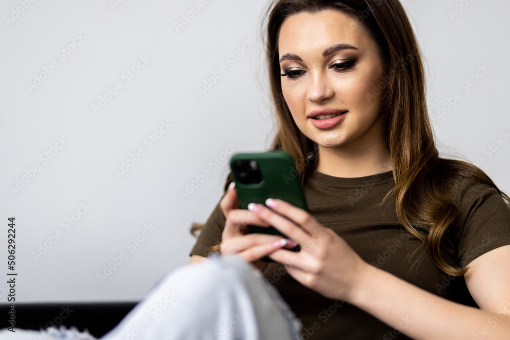 Smiling young woman using phone, sitting on couch at home, looking at smartphone screen Smiling young woman using phone, sitting on couch at home, looking at smartphone screen