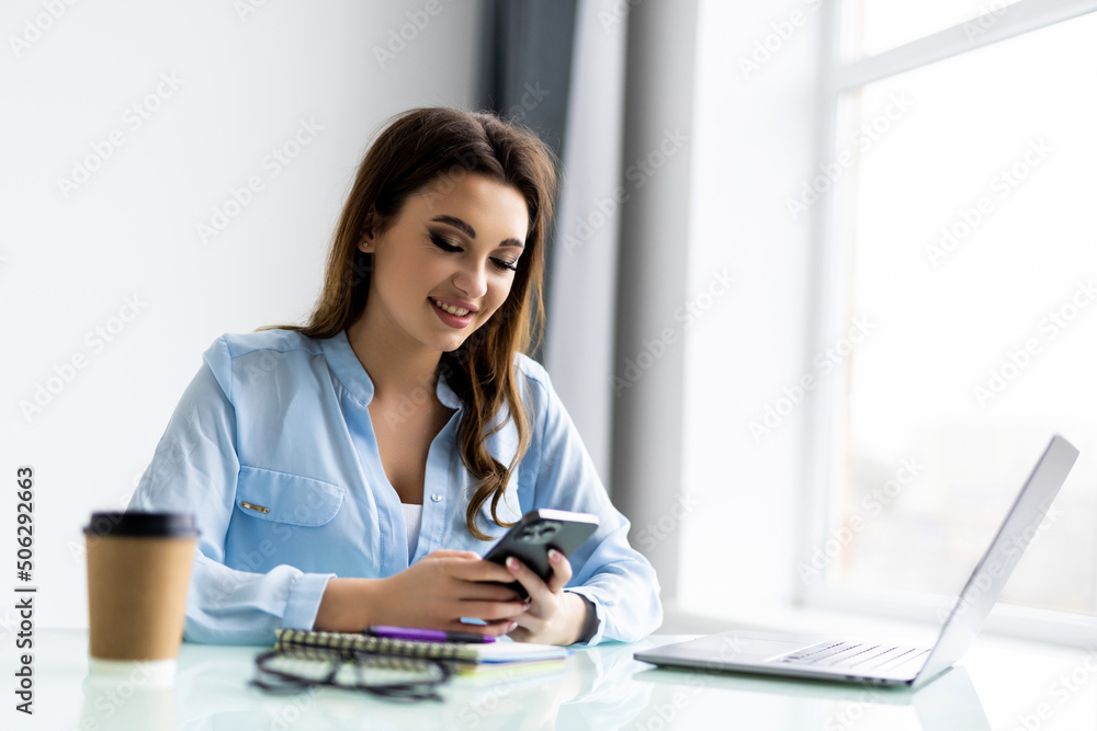 Freelance woman in glasses with mobile phone typing at laptop and working from home office with plants. Happy girl on workplace at the desk. Distance learning online education and work. Freelance woman in glasses with mobile phone typing at laptop and working from home office with plants. Happy girl on workplace at the desk. Distance learning online education and work.