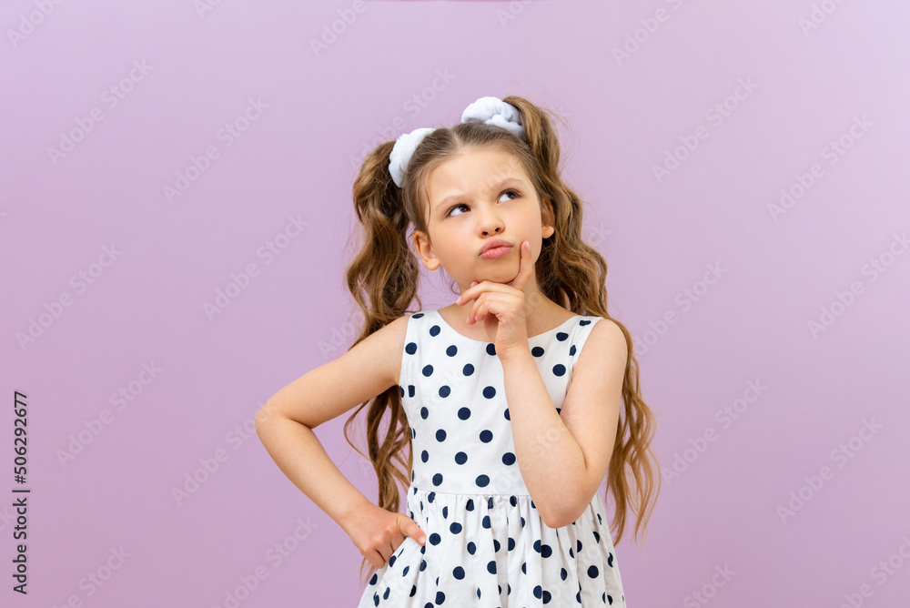 A thoughtful little girl looks up. a child in a dress on an isolated background. A thoughtful little girl looks up. a child in a dress on an isolated background.