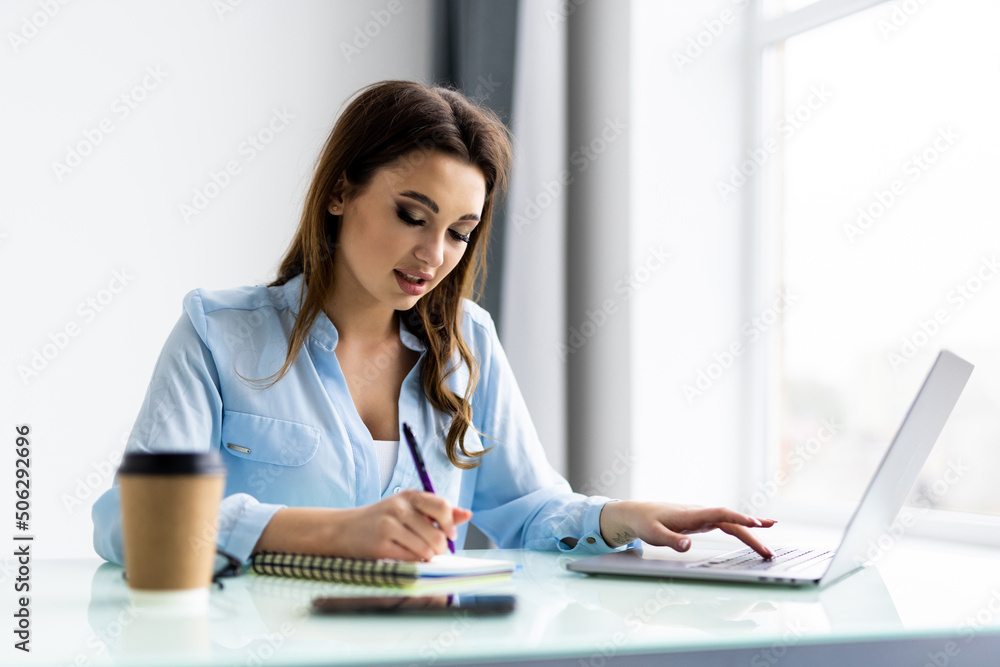 Business woman work on computers and write on notepad with pen to calculate financial statements within the office. Business woman work on computers and write on notepad with pen to calculate financial statements within the office.