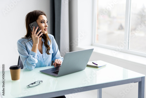 Portrait of beautiful executive woman making call while sitting at her workplace in front of laptop and working on new project.