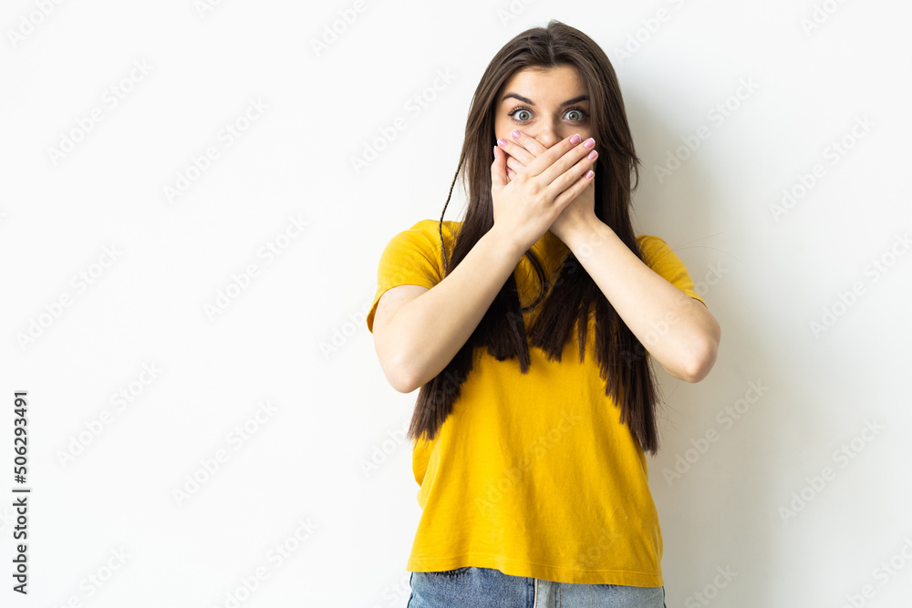 Portrait of a surprised young woman covering mouth with hands over white background Portrait of a surprised young woman covering mouth with hands over white background