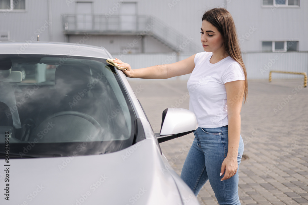Front view of attractive happy joyful female driver washing her car's headlights with special rag in self-service car wash Front view of attractive happy joyful female driver washing her car's headlights with special rag in self-service car wash