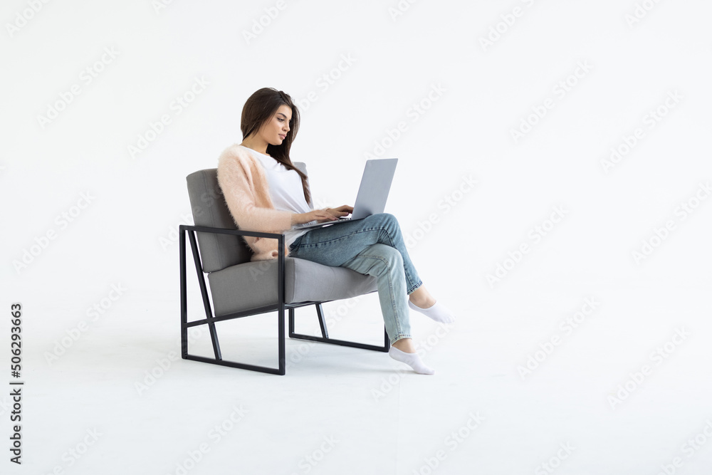Portrait of a young businesswoman sitting in a chair with laptop computer against white background Portrait of a young businesswoman sitting in a chair with laptop computer against white background