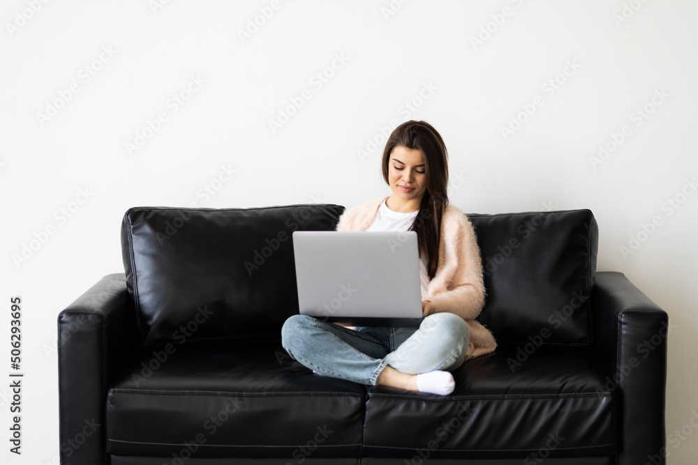 Smiling young woman using laptop, sitting on couch at home Smiling young woman using laptop, sitting on couch at home