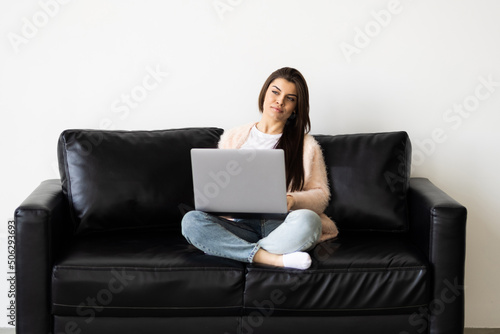 Photo of woman smiling and using laptop while sitting on couch in bright room