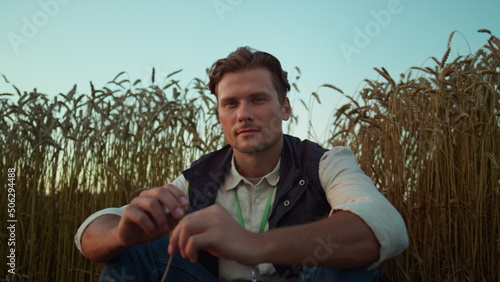 Portrait serious farmer posing at cultivated wheat field. Tired man rest alone.