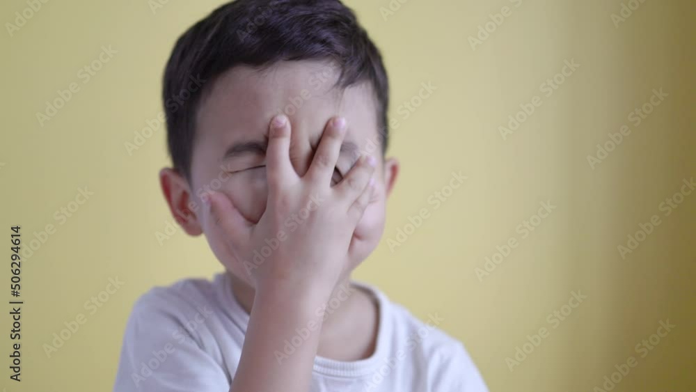 Cute boy smiling and covering his face on colour background. Facepalm Cute boy smiling and covering his face on colour background. Facepalm