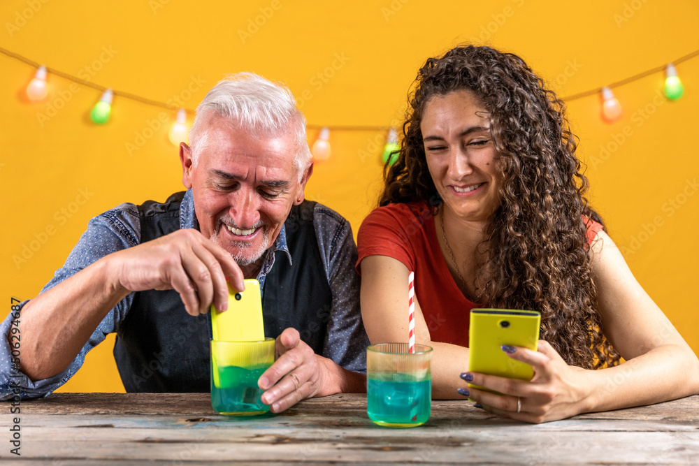 father and daughter have fun putting a smartphone into a glass full of a blue cocktail father and daughter have fun putting a smartphone into a glass full of a blue cocktail