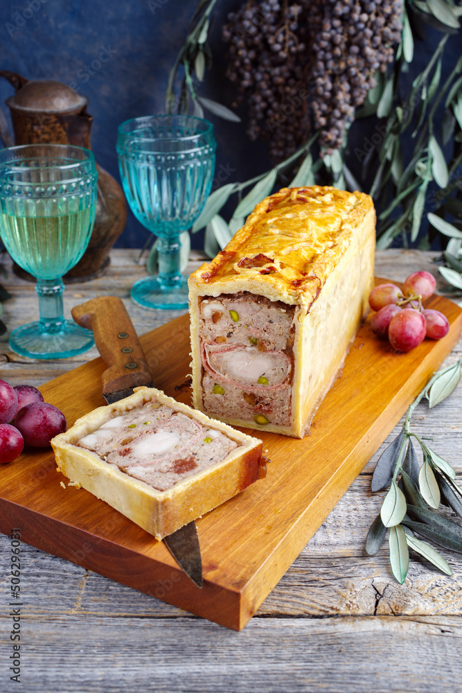 Traditional French Pate en croute with rabbit meat and pork filet serviert with grapes as close-up on a modern design wooden board