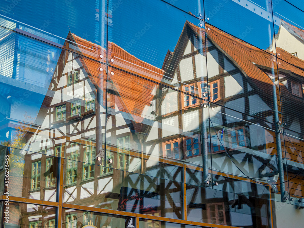 Obraz premium Ein Fachwerkhaus spiegelt sich in der verglasten Fassade eines Gebäudes im Sonnenschein