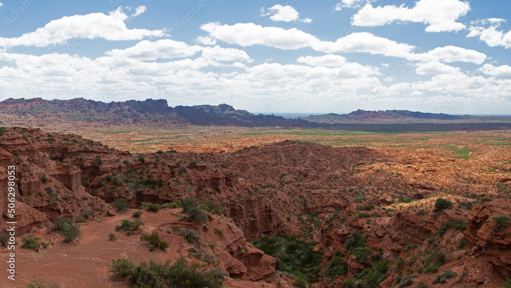 The red canyon. Panorama view of the arid desert, sandstone and rocky cliffs and mountains under a blue sky with clouds.