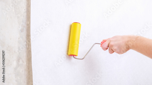 A man rolls out a canvas of white wallpaper with a suture yellow roller. Removing air bubbles and glue. Wallpapering. Repair of a room, apartment, house.