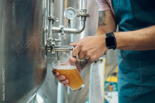 Photographie Close shot of a man filling glass of beer on a tap in brewery