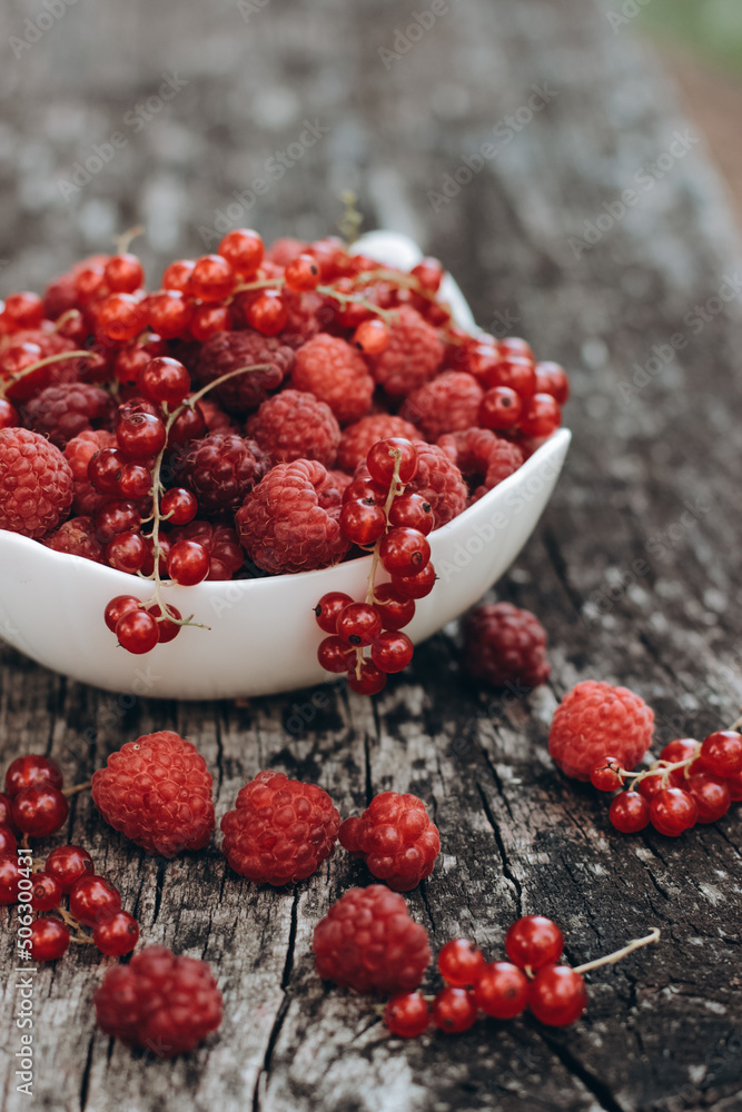 White bowl with fresh organic raspberry and red currant. Placed on  natural gray wood background. Tasty snack or fresh topping for your desserts