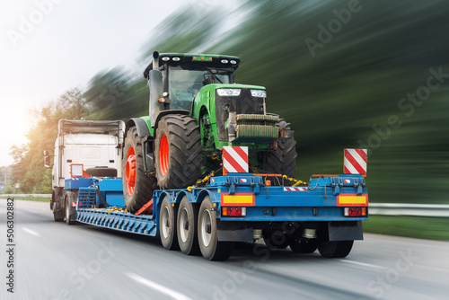 POV heavy industrial truck semi trailer flatbed platform transport one big modern farming tractor machine on common highway road at bright day sky. Agricultural equipment transportation service work