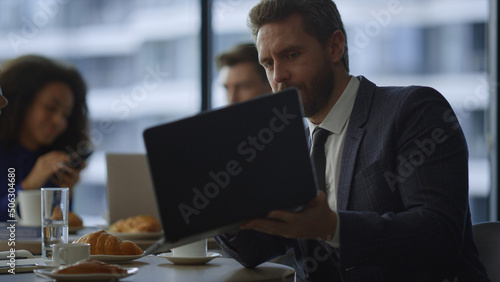 Busy manager showing laptop computer to business colleague in restaurant cafe.