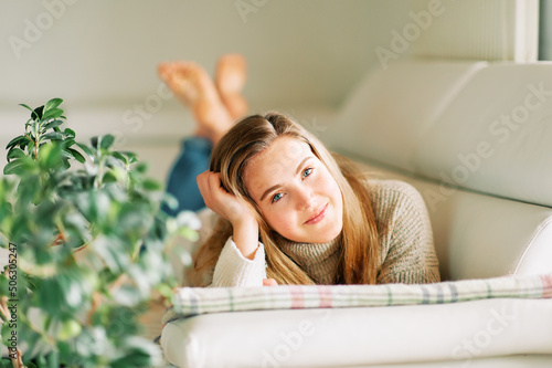 Indoor portrait of young cute 20 year old girl lying on couch  wearing warm pullover