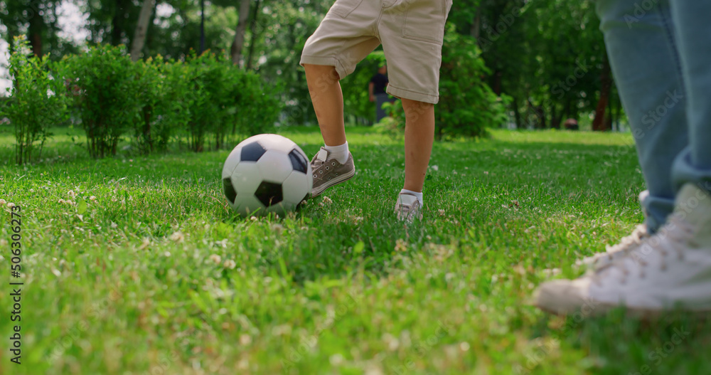 Unknown boy legs making soccer exercise closeup. Son training football with dad. Unknown boy legs making soccer exercise closeup. Son training football with dad.