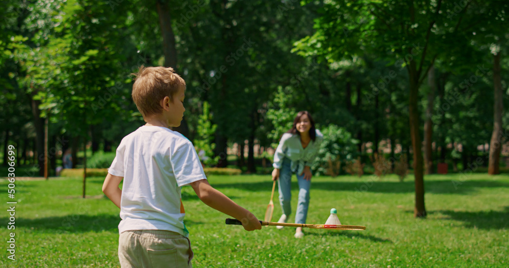 Fototapeta premium Joyful mother play badminton with son in park. Happy family have fun outdoor.