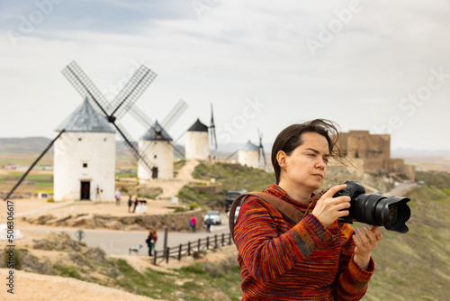 Female traveler with passion for photography walking along Cerro Calderico ridge in Consuegra in springtime, focused on taking pictures of nature and ancient windmills with professional camera.. photo